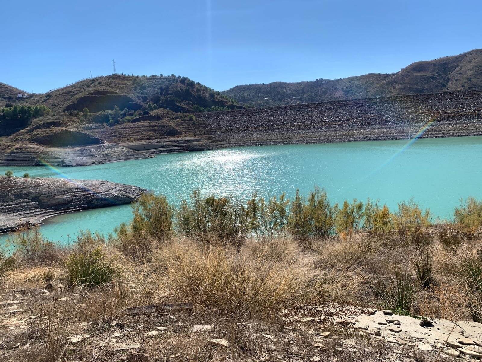 Overlooking Lake Vinuela. It is a sunny day and the sky is blue. The sun is reflecting off of the blue water in the lake.