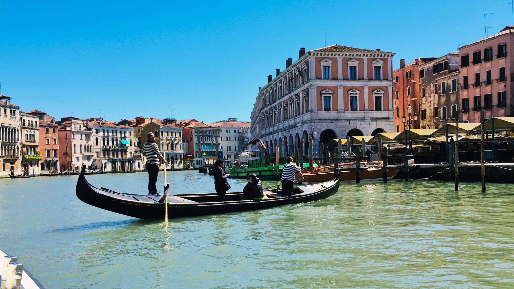 Image shows a Gondola crossing the water on a sunny day in Venice.